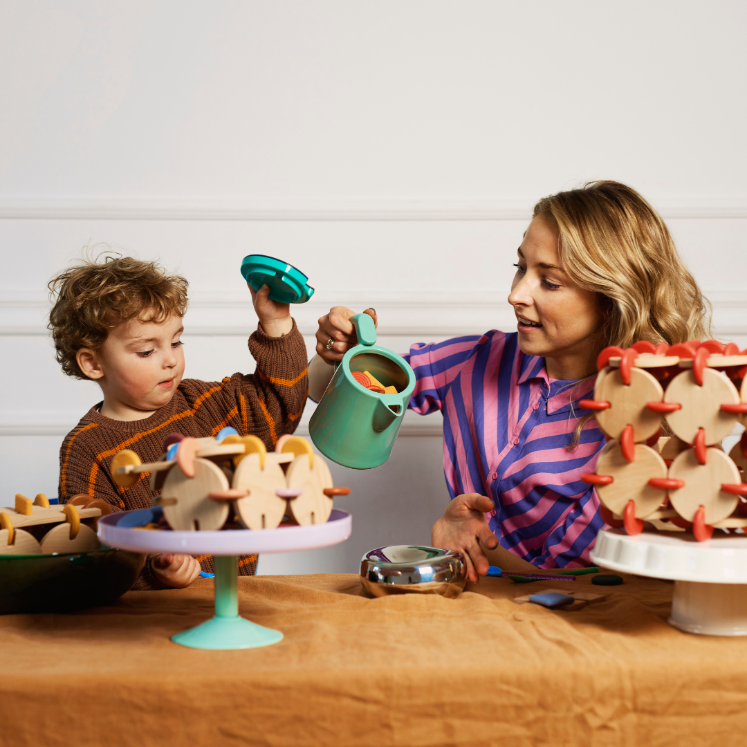 Adult and child pour silicone connectors beside BAVVIC wooden builds — playful construction toy