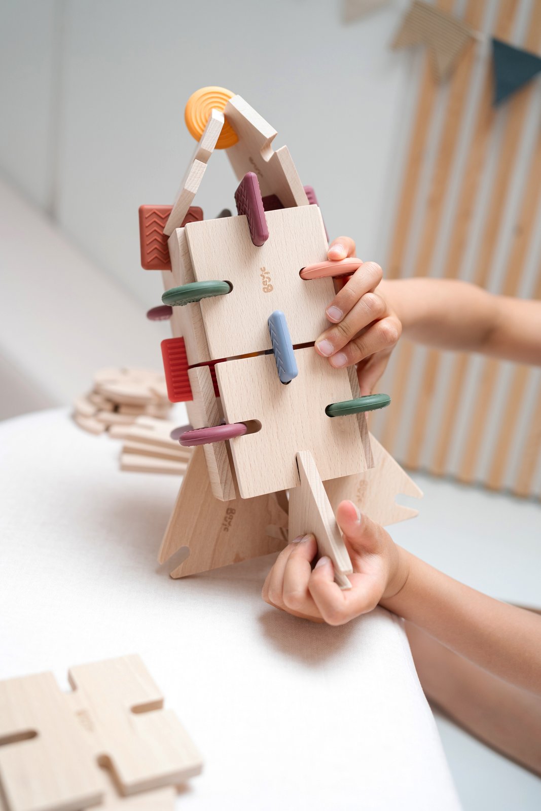 Child's hands building a tall tree-like tower from BAVVIC beech-wood pieces and colourful silicone connectors on a white table