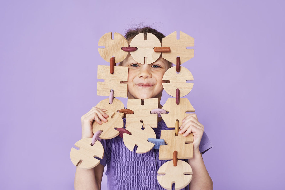 Child peeking through a square frame built from BAVVIC beech-wood pieces and silicone connectors against a lilac backdrop